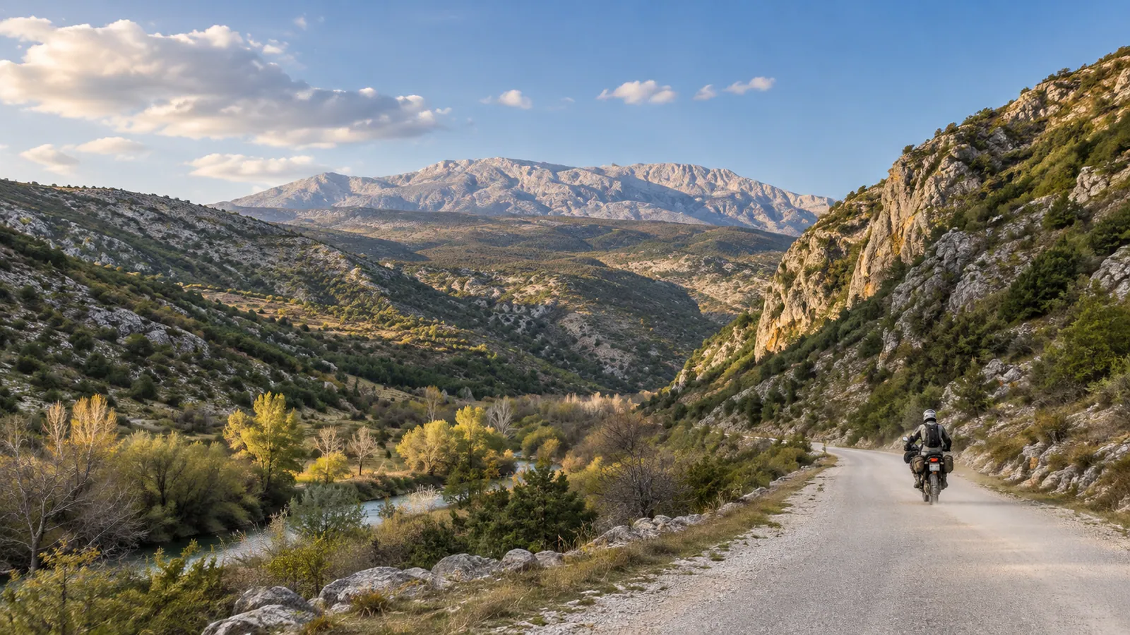 An adventure rider follows a pale gravel road through the broad Krčić canyon beneath a limestone ridge.