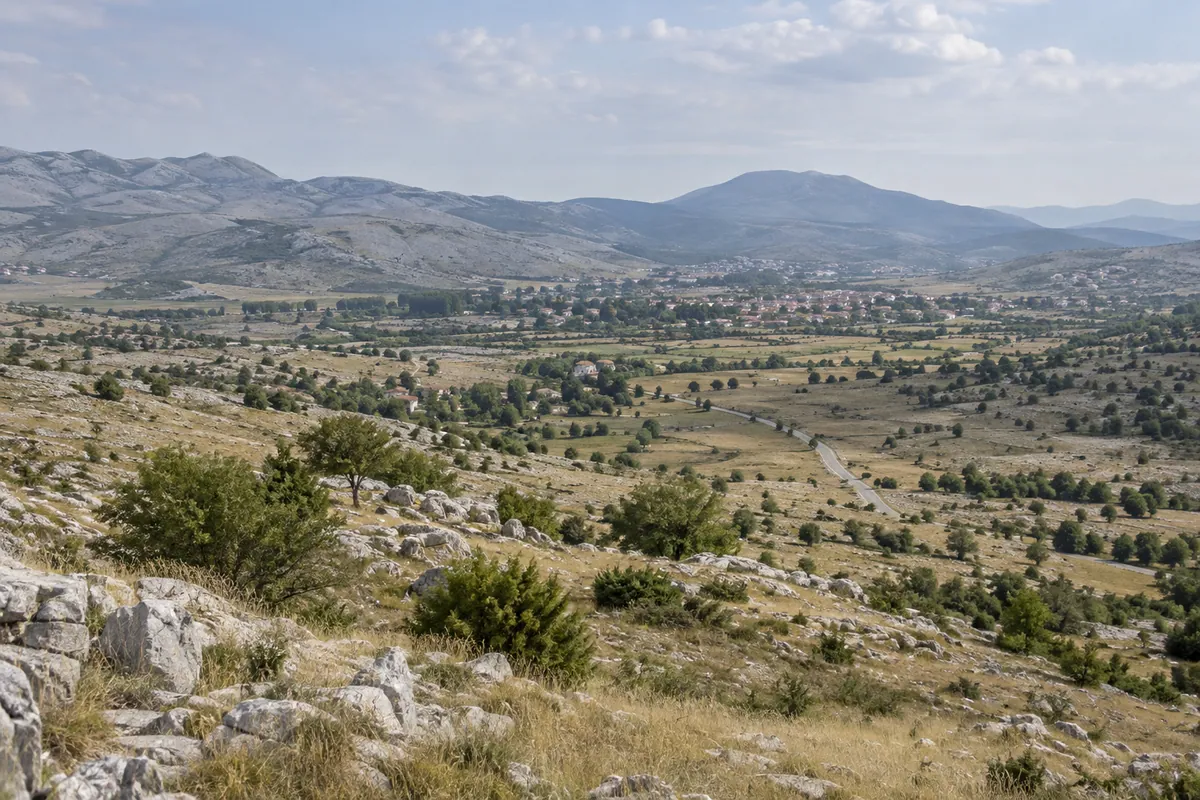 Open karst country and a distant road surround Nevesinje beneath eastern Herzegovinian hills.
